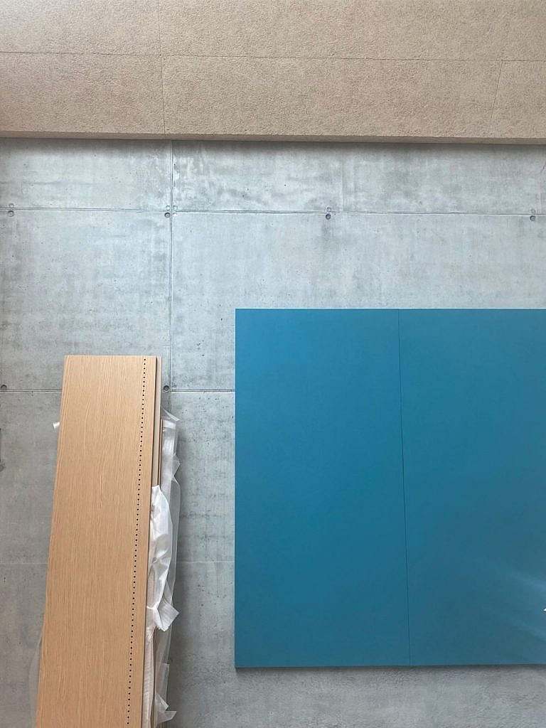 Den insitu-støbte beton får lov at stå råt, men får modspil og blødes op af elementer og træ og farver. Her er det en stor blå opslagstavle. Brugen af farver i byggeri er en grønlands byggeskik.